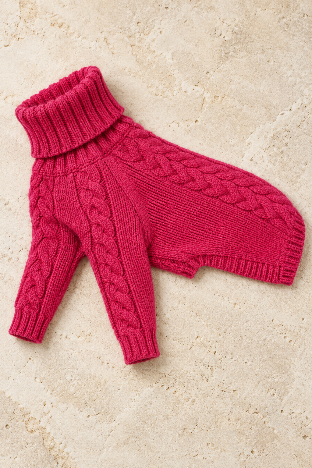Rose pink cable knit dog sweater laid flat on limestone