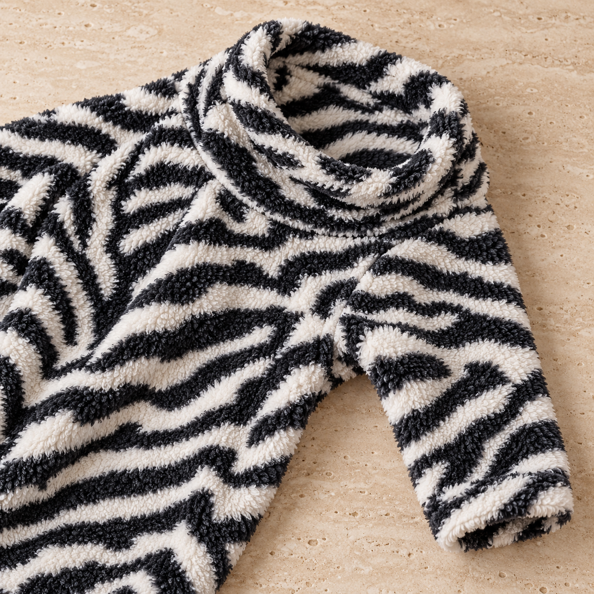 Close-up of zebra coral fleece collar, shoulder and sleeve laid on cream stone
